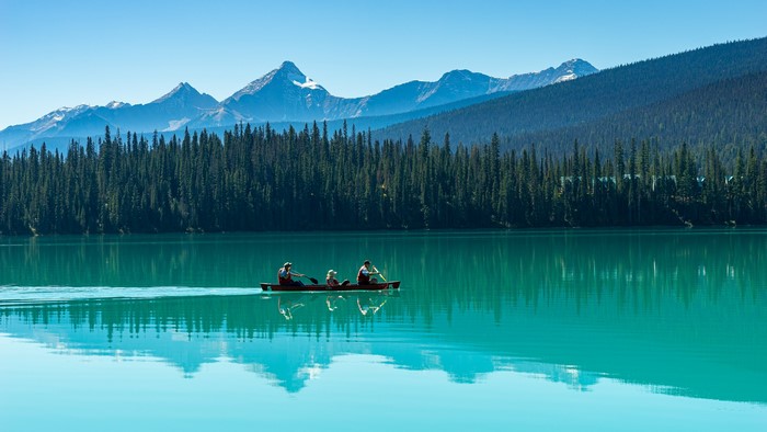 Canoeists on a turquoise lake with mountains and forest