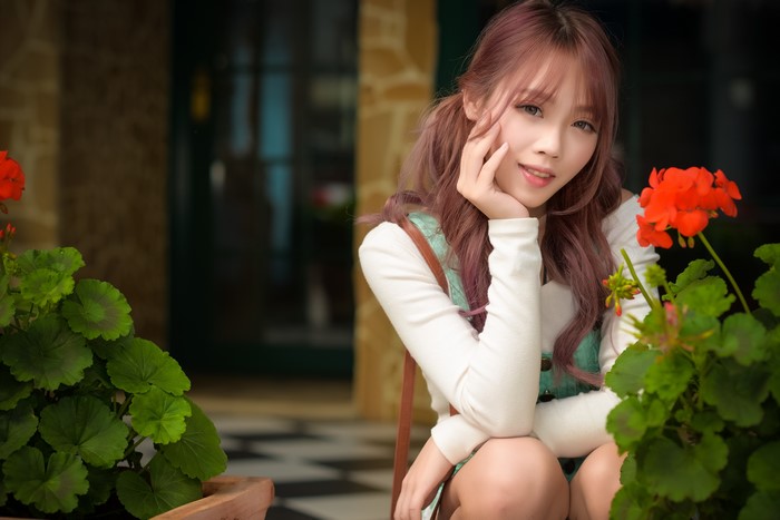 Asian Woman Sitting Among Green Plants and Red Flowers