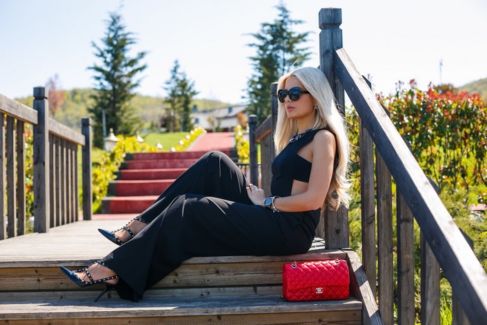 Woman in black jumpsuit sitting on wooden stairs with red handbag