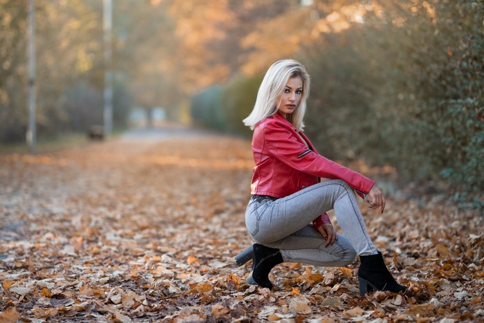 Blonde girl in red jacket and jeans posing in autumn foliage
