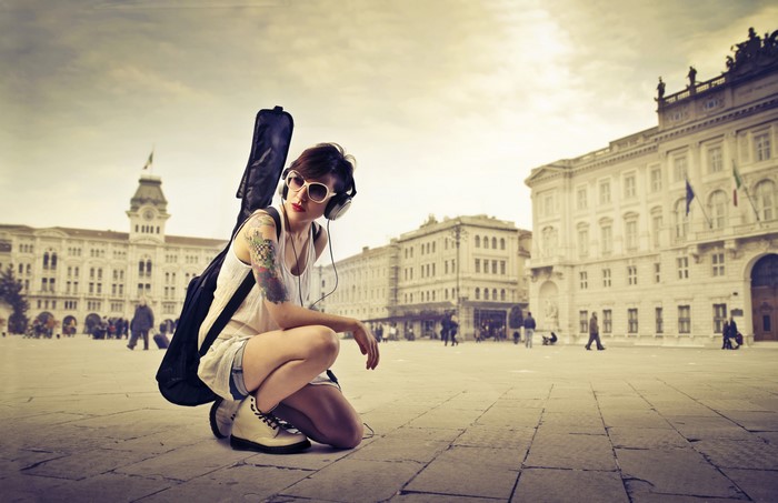 Girl with guitar and headphones in town square