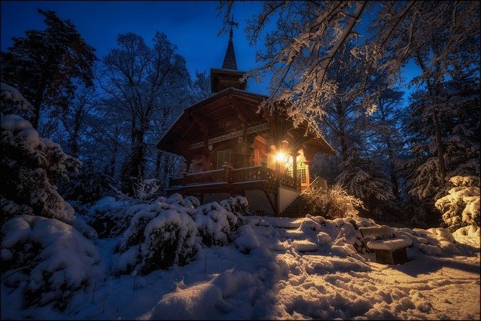 Wooden house in a snowy forest at dusk
