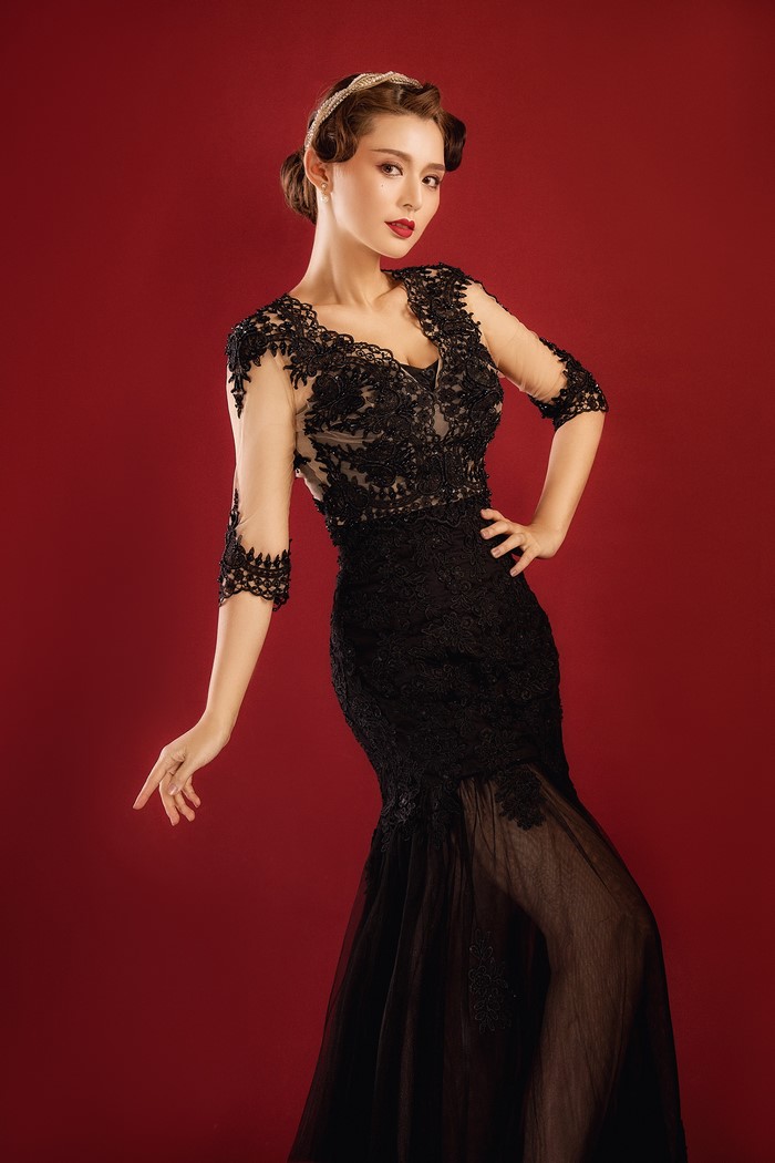 Woman in black lace dress posing against red background