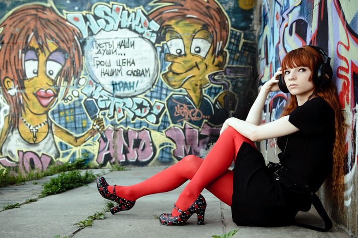 Redhead girl with headphones sitting by graffiti wall