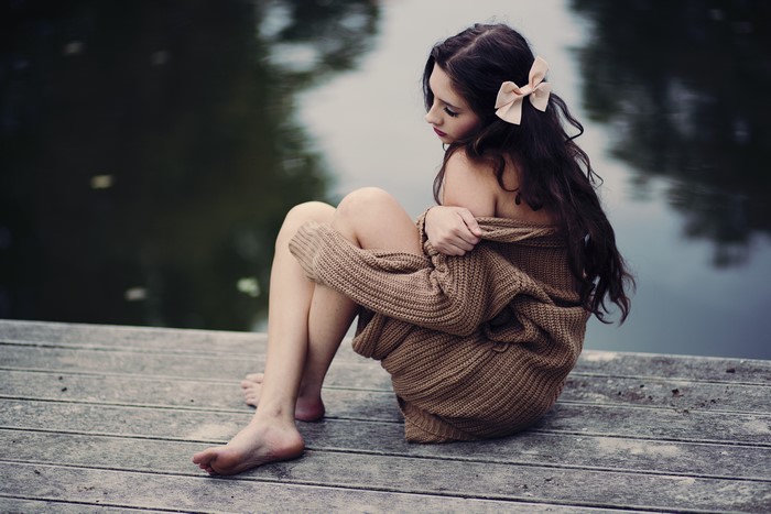 Brunette girl in sweater sitting on a dock