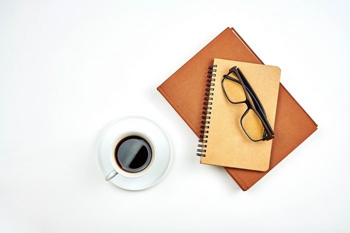Coffee cup, notepad, glasses, and book on white background