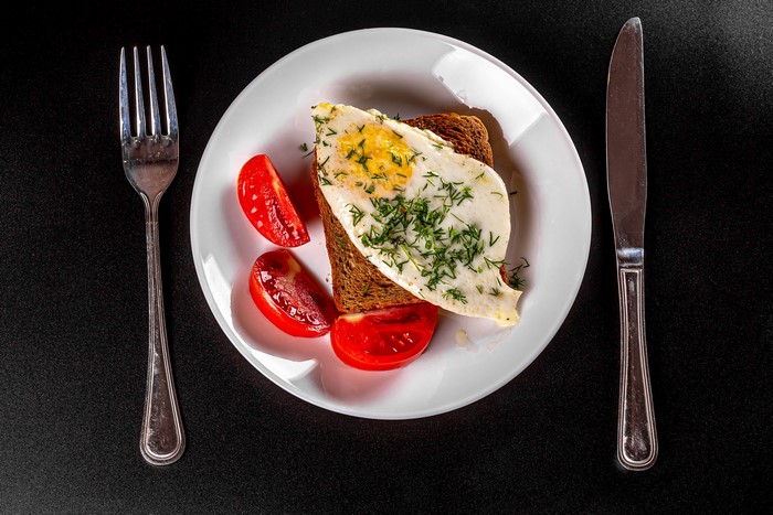 Fried egg on toast with tomatoes, fork, and knife