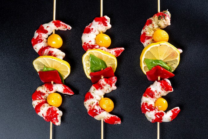 Shrimp skewers with lemon and red pepper on a dark background