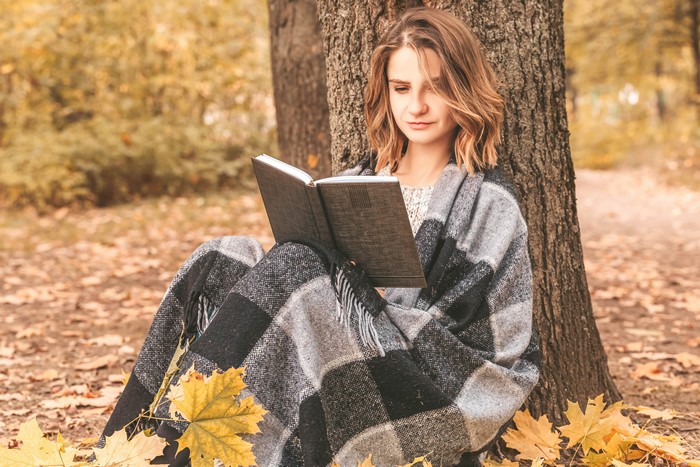 Woman reading a book under a tree in autumn