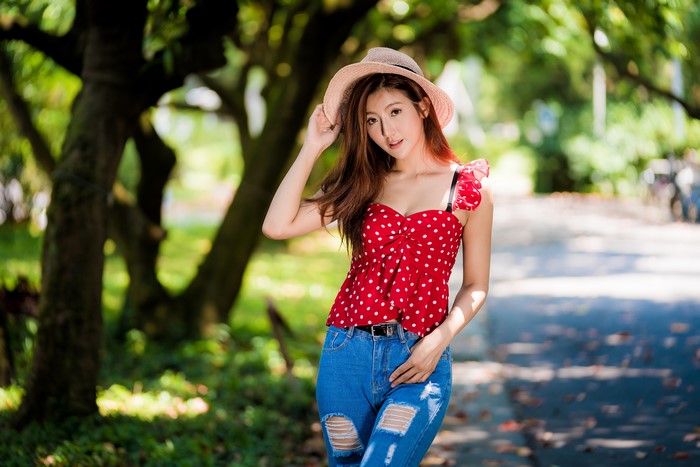 Asian woman in red polka dot blouse and ripped jeans wearing a hat