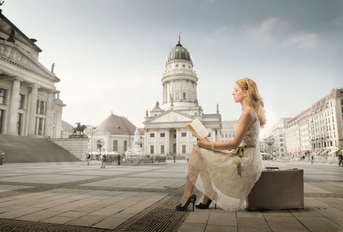 Woman reading a book on a suitcase in a town square