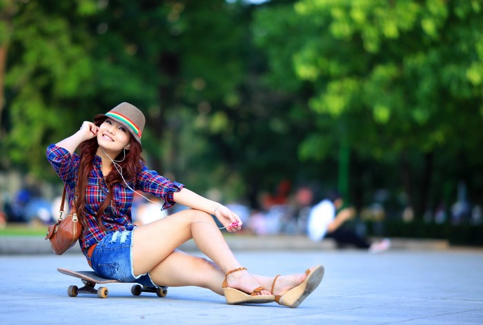 Asian girl with skateboard wearing hat and shorts