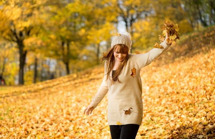 Woman in sweater and winter hat throwing leaves