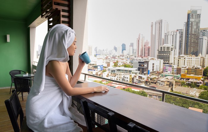 Woman in towel with mug on balcony overlooking city