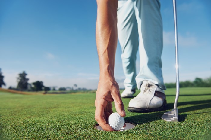Golf ball being placed in hole on green