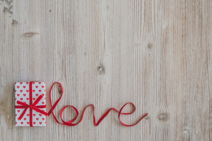 Gift with red ribbon spelling "Love" on wooden background