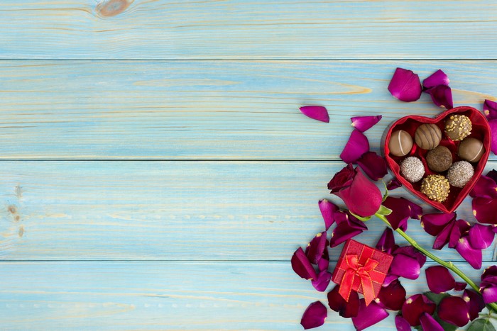 Valentine's Day heart box of chocolates, rose, and petals on wood