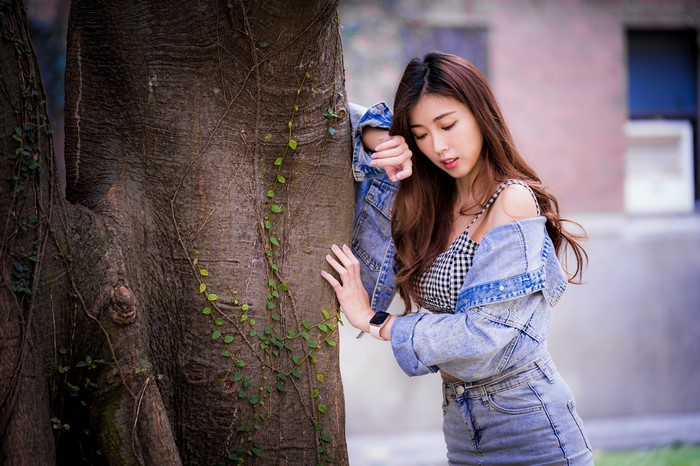 Asian woman in denim jacket leaning on tree trunk