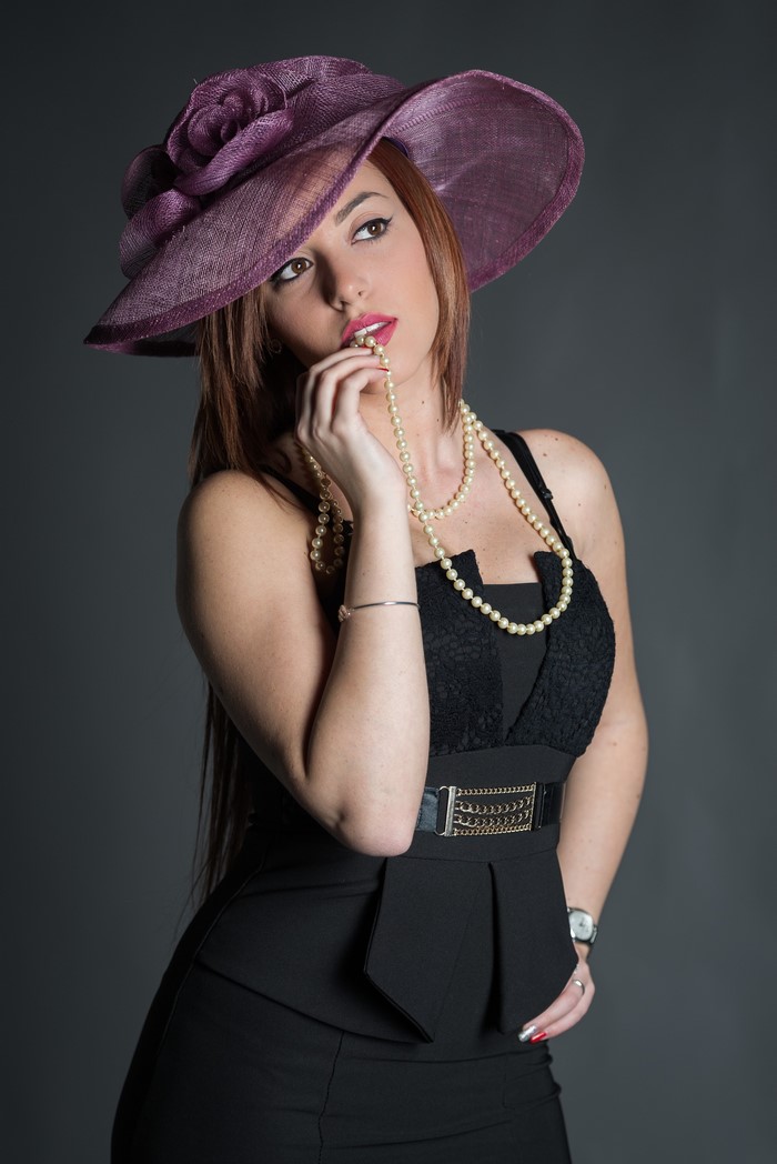 Woman in purple hat and black dress with pearls