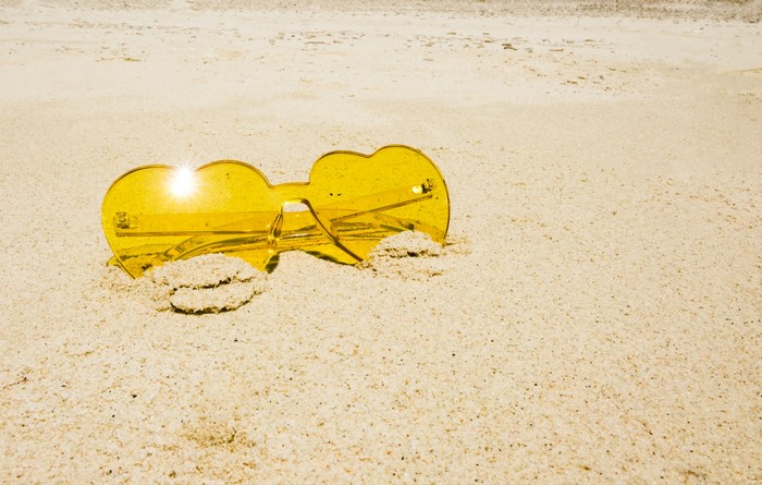 Yellow sunglasses on sand with sun glare