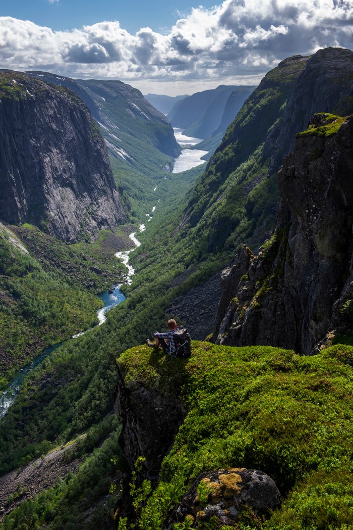 Man sitting on a cliff overlooking a Norwegian valley