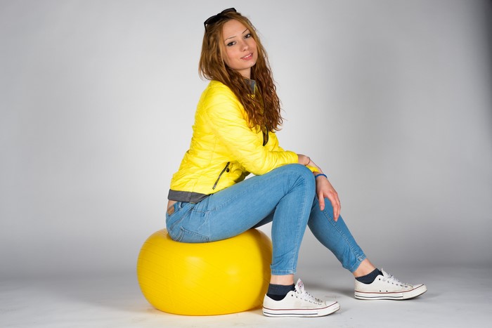Young woman with brown hair sitting on a yellow ball