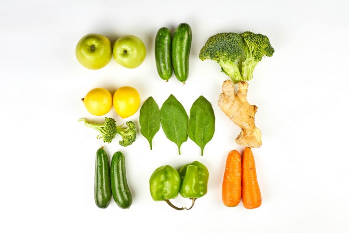 Apples, lemons, cucumbers, broccoli, spinach, ginger, bell peppers, and carrots on a white background