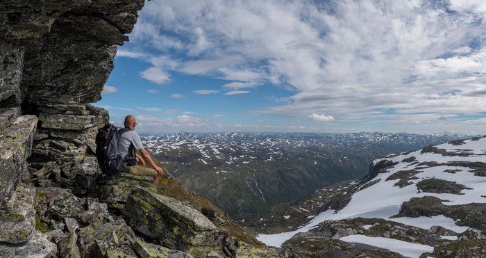 Man sitting on a rocky outcrop overlooking a snowy mountain panorama