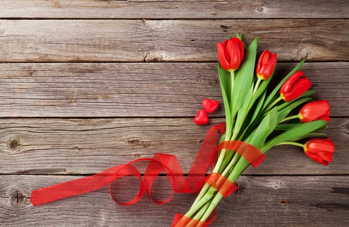 Red tulips with ribbon and hearts on wood planks