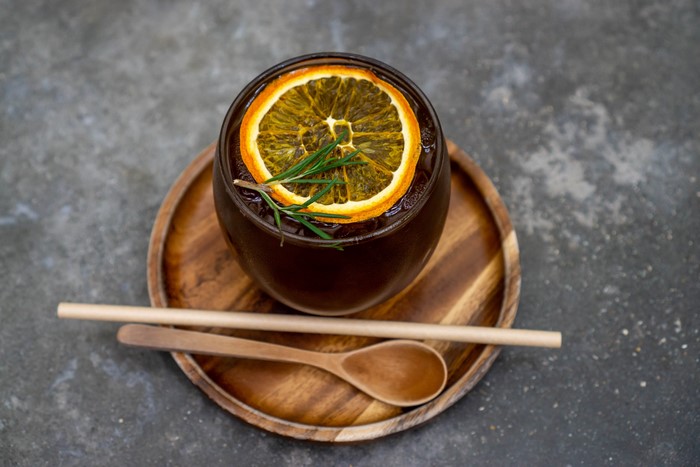 Iced tea with orange slice and rosemary on a wooden tray