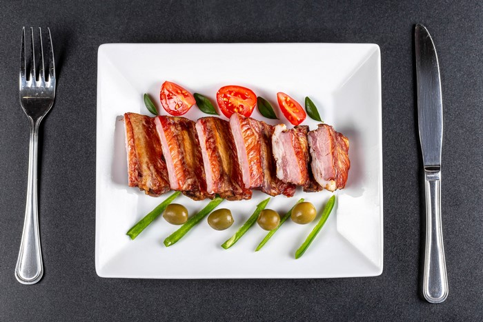 Ribs with tomatoes and olives on a plate with fork and knife