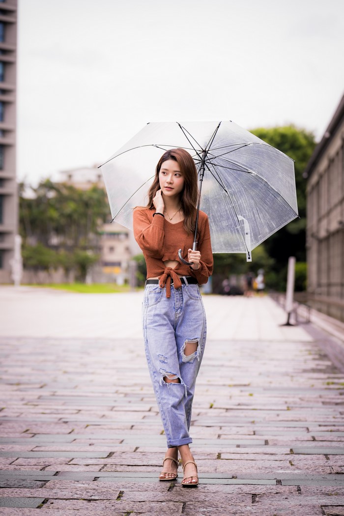 Asian woman holding an umbrella, wearing jeans and a sweater