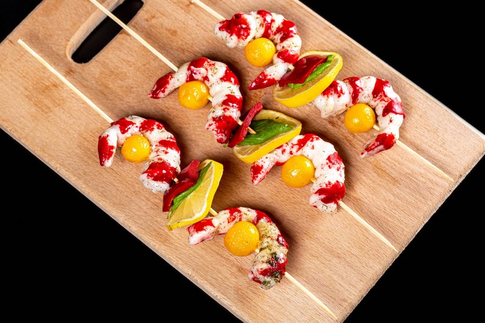 Shrimp skewers with lemons and tomatoes on a cutting board