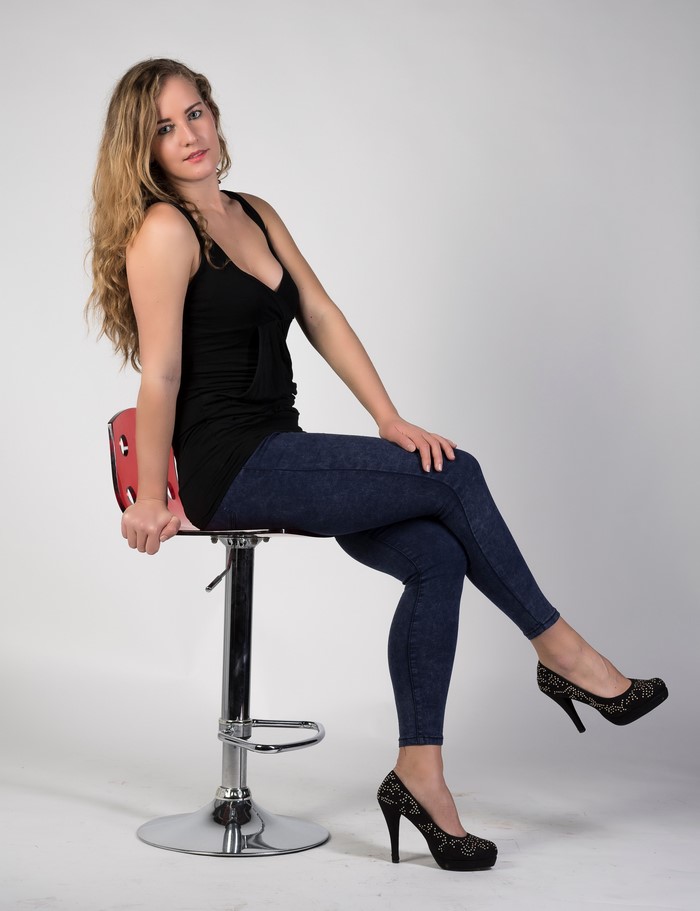 Alexandra sitting on a stool wearing jeans and stilettos