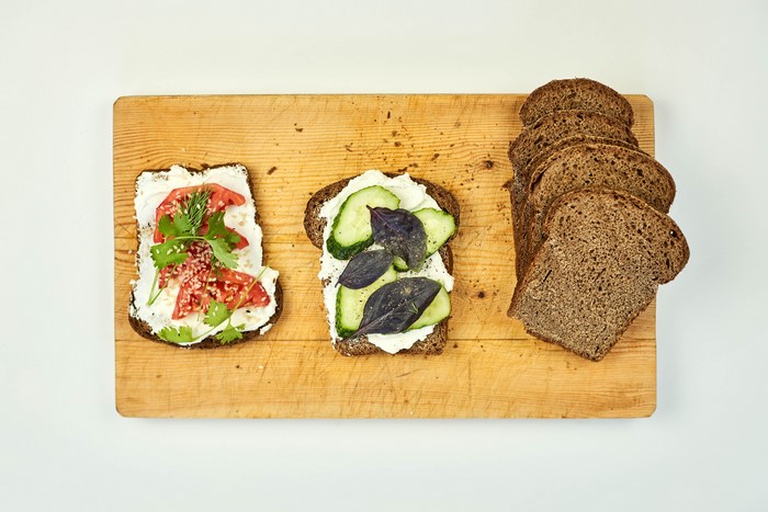 Bread slices with cream cheese, tomatoes, cucumbers, and herbs on a cutting board