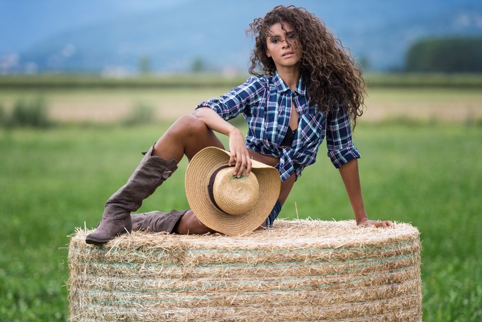 Woman in plaid shirt and boots on hay bale