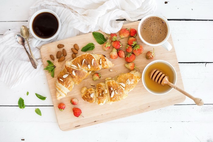 Croissant, strawberries, honey, and coffee on a wooden tray
