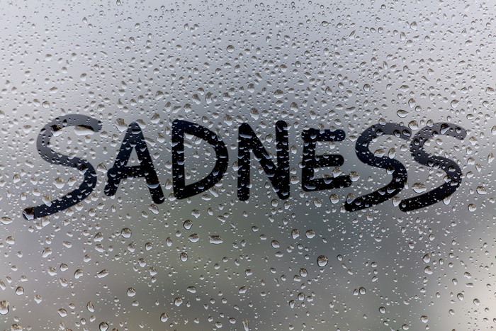 SADNESS written on glass with water drops