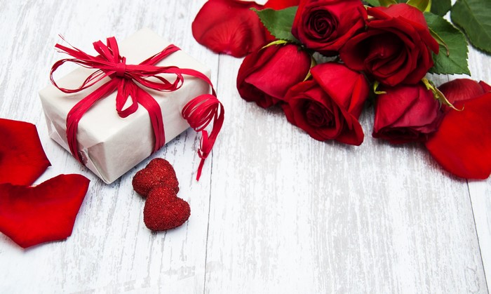 Gift box with red roses and petals on a wooden table