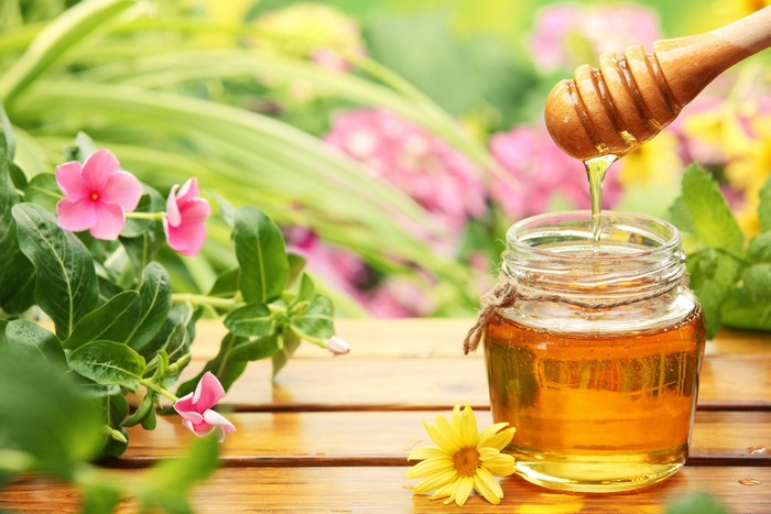 Honey in a jar with a honey dipper and flowers