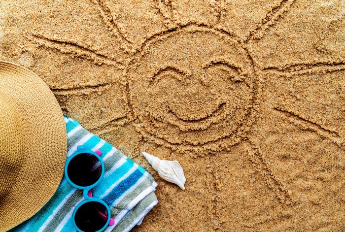 Sun drawn in sand with beach accessories