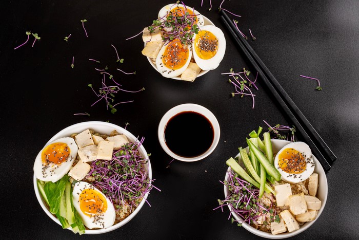 Three bowls of porridge with eggs, tofu, and sprouts