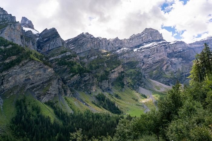Layered mountains with green slopes and forests under a cloudy sky