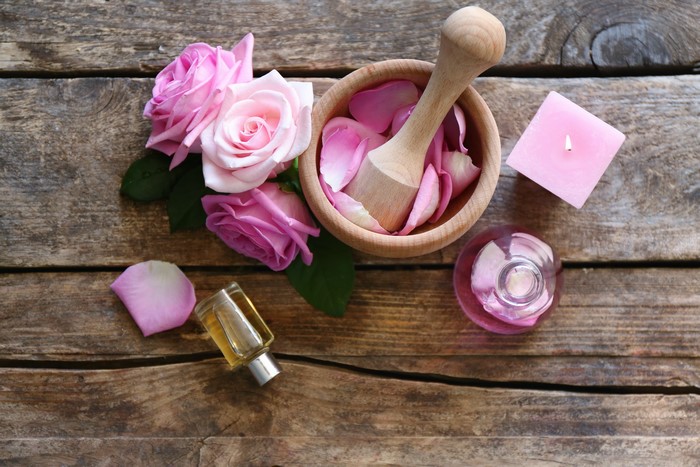 Roses, Mortar and Pestle, Candle, and Perfume Bottles on Wood