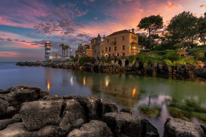 Lighthouse and houses on rocky coast at sunset in Cascais, Portugal