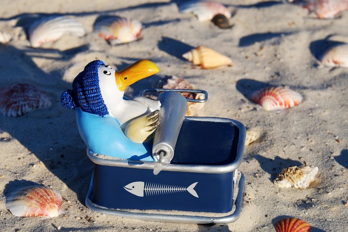 Toy penguin with a can of fish on a beach