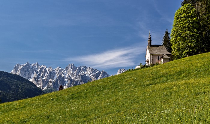 Church on a grassy hill with Alps mountains