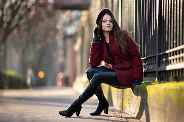 Woman in red coat and beret sitting by fence