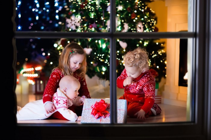 Three Children Opening Christmas Gifts by the Tree