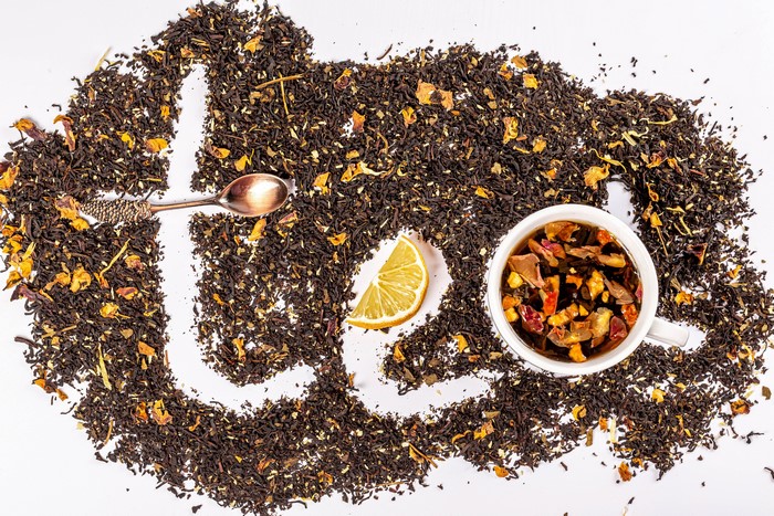 Tea leaves arranged to spell 'tea' with a cup, spoon, and lemon slice
